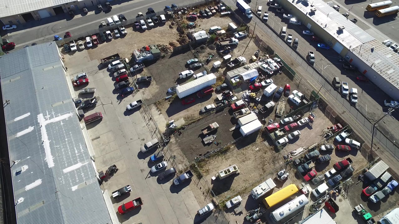Overhead view of industrial sheds, parked vehicles, trailers, and dirt yard.