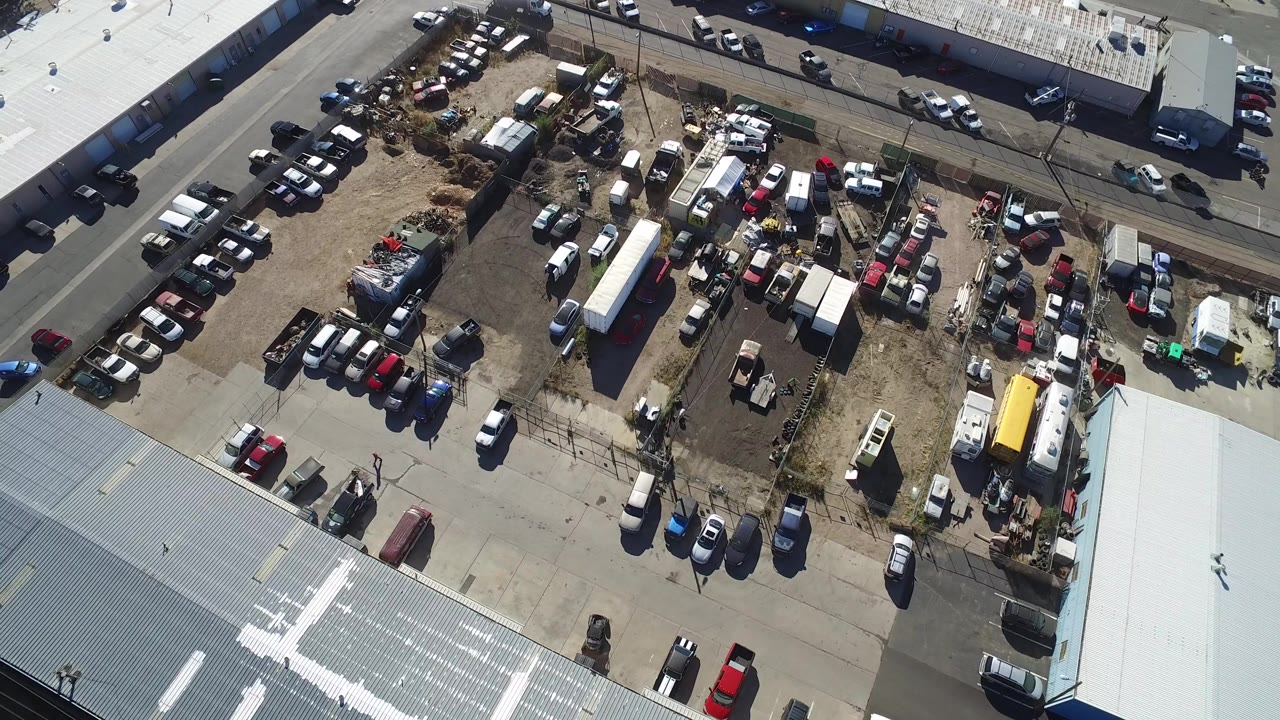 Overhead view of a vehicle-filled lot beside low industrial buildings.