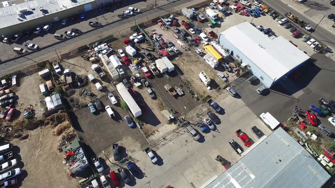 High aerial frame over Hidden Lake, Colorado, showing white-roofed buildings, parked cars, trailers, dirt yard areas, and no visible people.