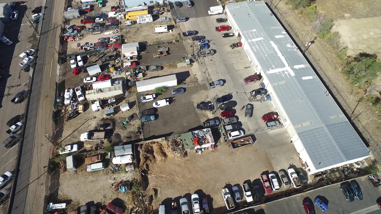 Top-down industrial lot with trucks, cars, debris, and road frontage.