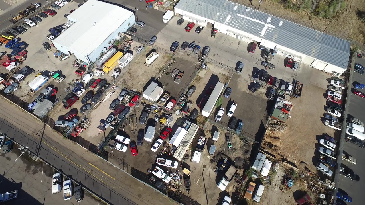 Top-down view of a workshop property with cars, trucks, trailers, and boundary walls.