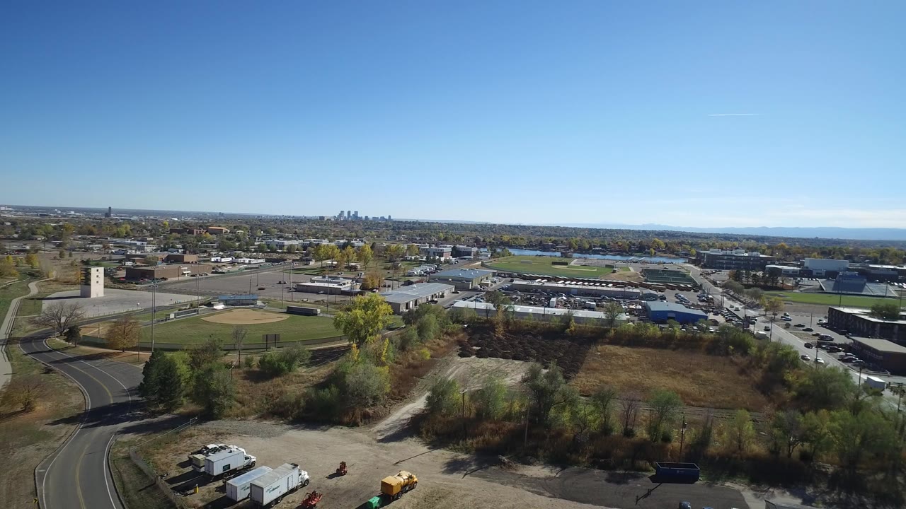 Opening aerial frame over Hidden Lake, Colorado showing a curved road, sports fields, low buildings, autumn trees, distant skyline, and no visible people.