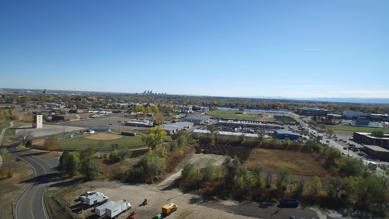 Aerial frame in Hidden Lake, Colorado with a road and open lots in the foreground, ball fields and low buildings in the middle distance, and no visible people.