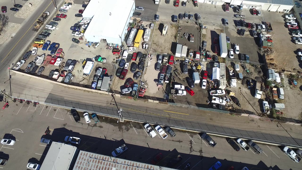 High overhead frame in Hidden Lake, Colorado showing industrial rooftops, a packed vehicle yard, adjacent roads, utility poles, and no visible people.