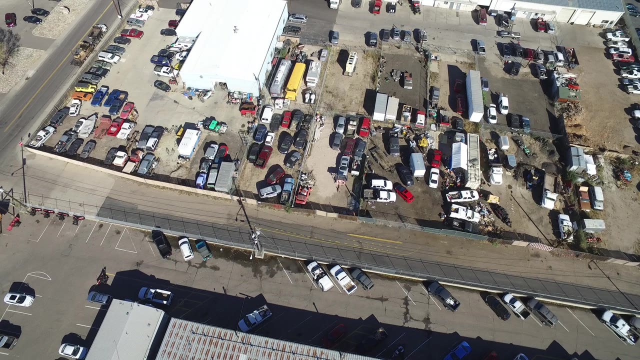 Overhead Hidden Lake, Colorado view centered on parked cars around white-roofed industrial buildings, with a cross street and no visible people.