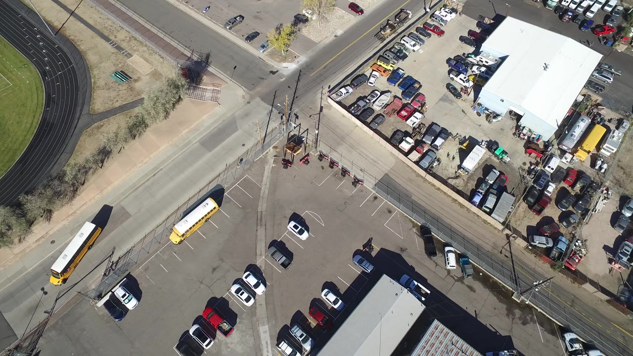 Overhead shot of parked vehicles, school buses, a road crossing, and a track field corner.