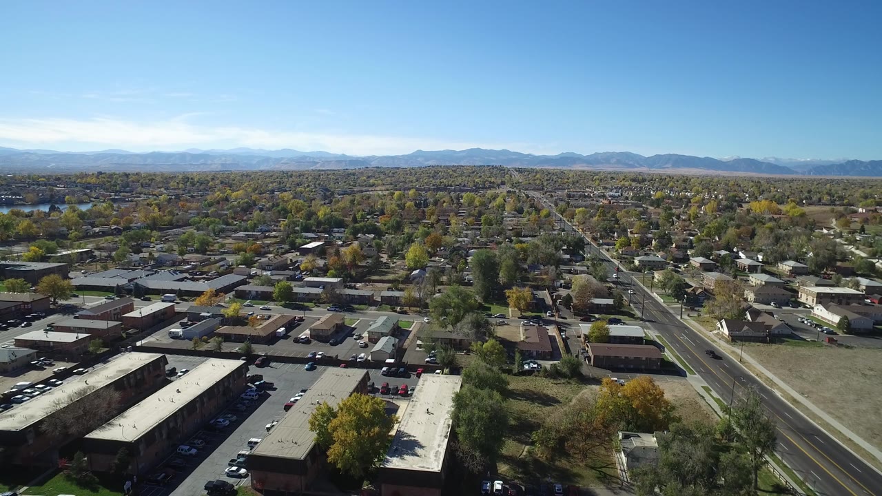 Suburban aerial with rooftops, cars, trees, road grid, and mountain horizon.