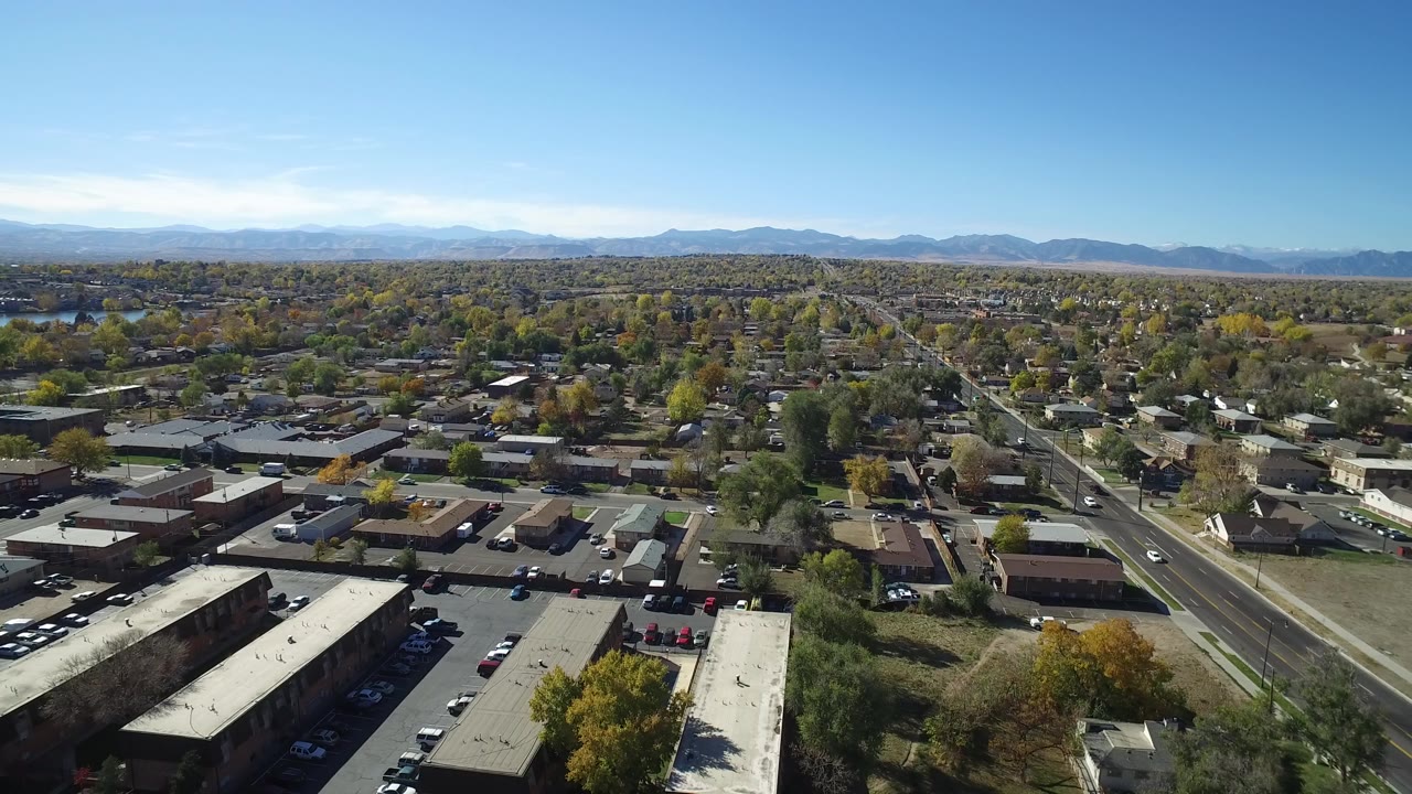 Aerial view over low-rise buildings, streets, trees, and distant mountains.