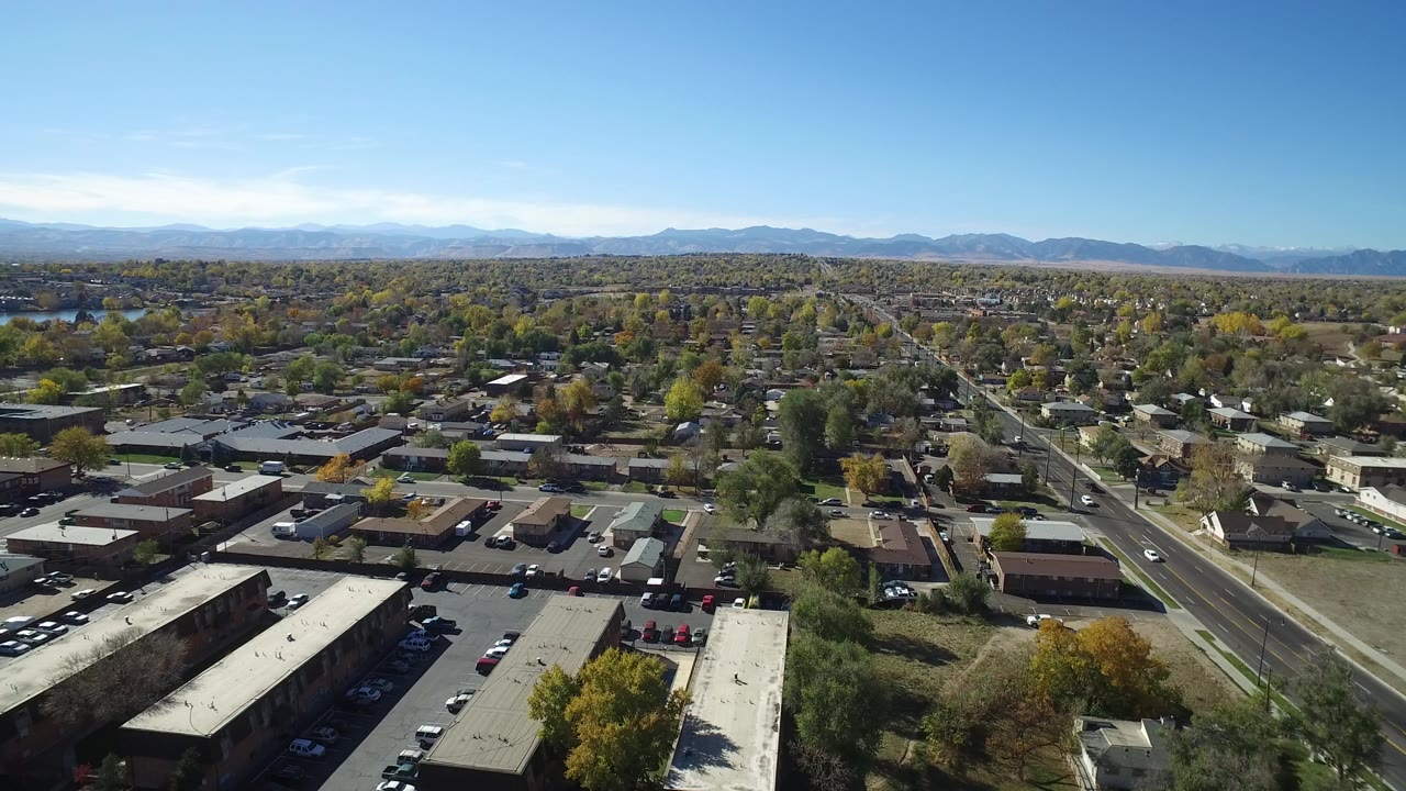 Aerial view in Hidden Lake, Colorado looking across commercial rooftops and parking areas toward a broad residential grid with autumn trees and distant mountains.