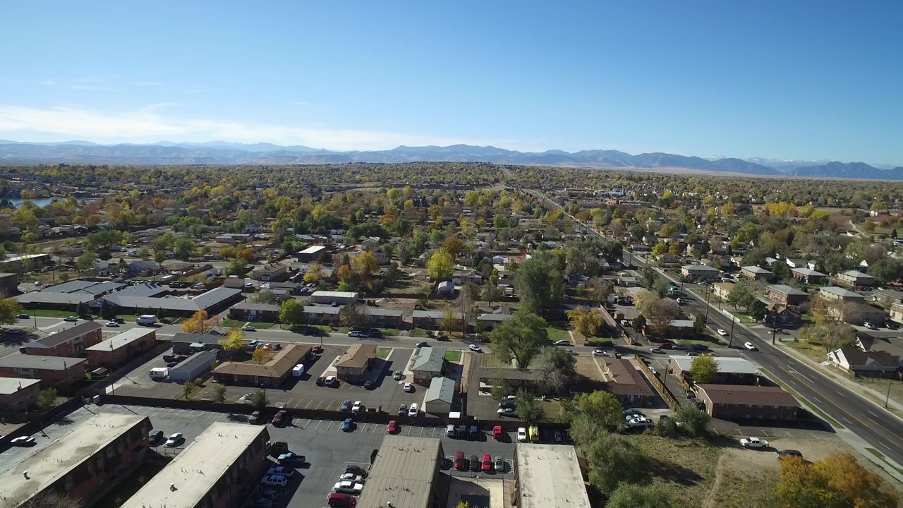 Aerial view over commercial roofs, a road, homes, trees, and distant mountains.
