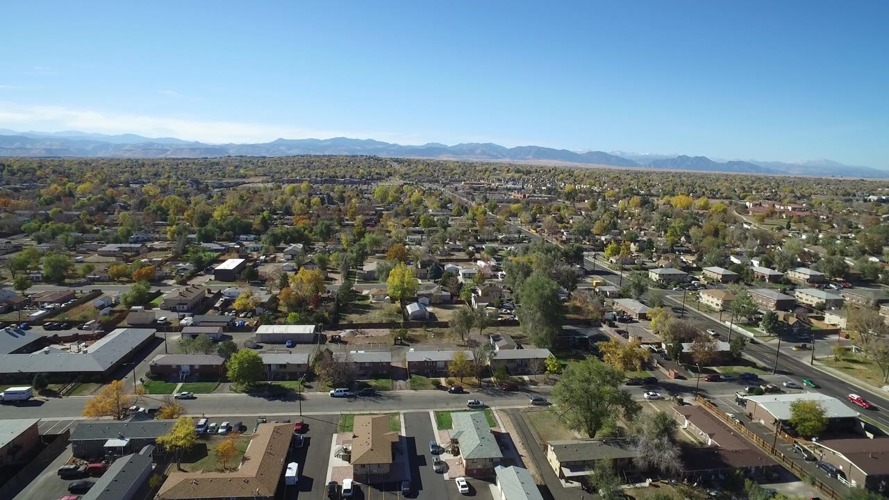 Aerial view over suburban homes, streets, trees, and distant mountains.