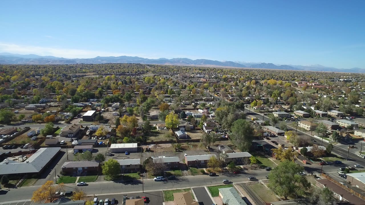 Aerial view over suburban houses, streets, trees, and distant mountains.
