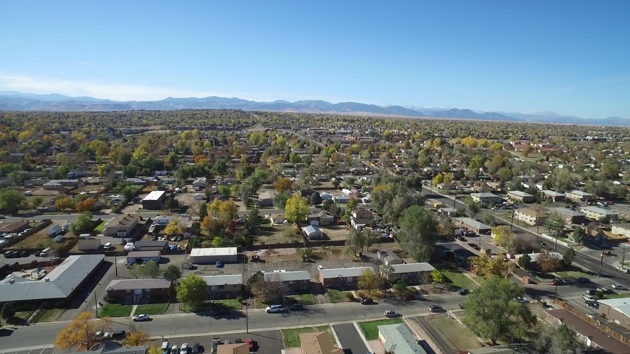 Aerial view across Hidden Lake, Colorado rooftops and neighborhood streets, with autumn-colored trees and mountains along the horizon, no visible people.
