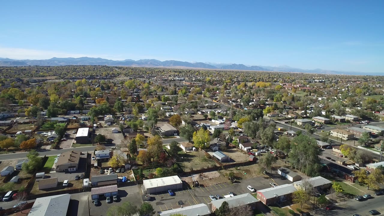 Opening aerial frame over Hidden Lake, Colorado showing residential rooftops, tree-lined streets, distant mountains, and no visible people.