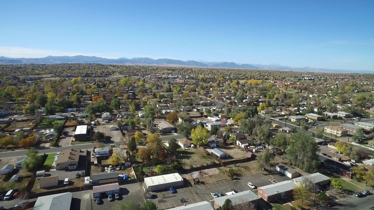 Aerial suburban panorama with houses, trees, roads, and a blue sky.