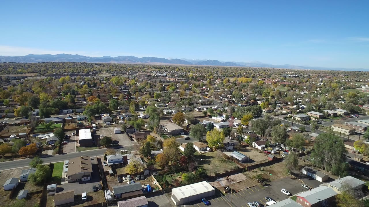 High aerial view over Hidden Lake, Colorado, showing low-rise homes, tree-lined roads, open lots, distant hills, and no visible people.