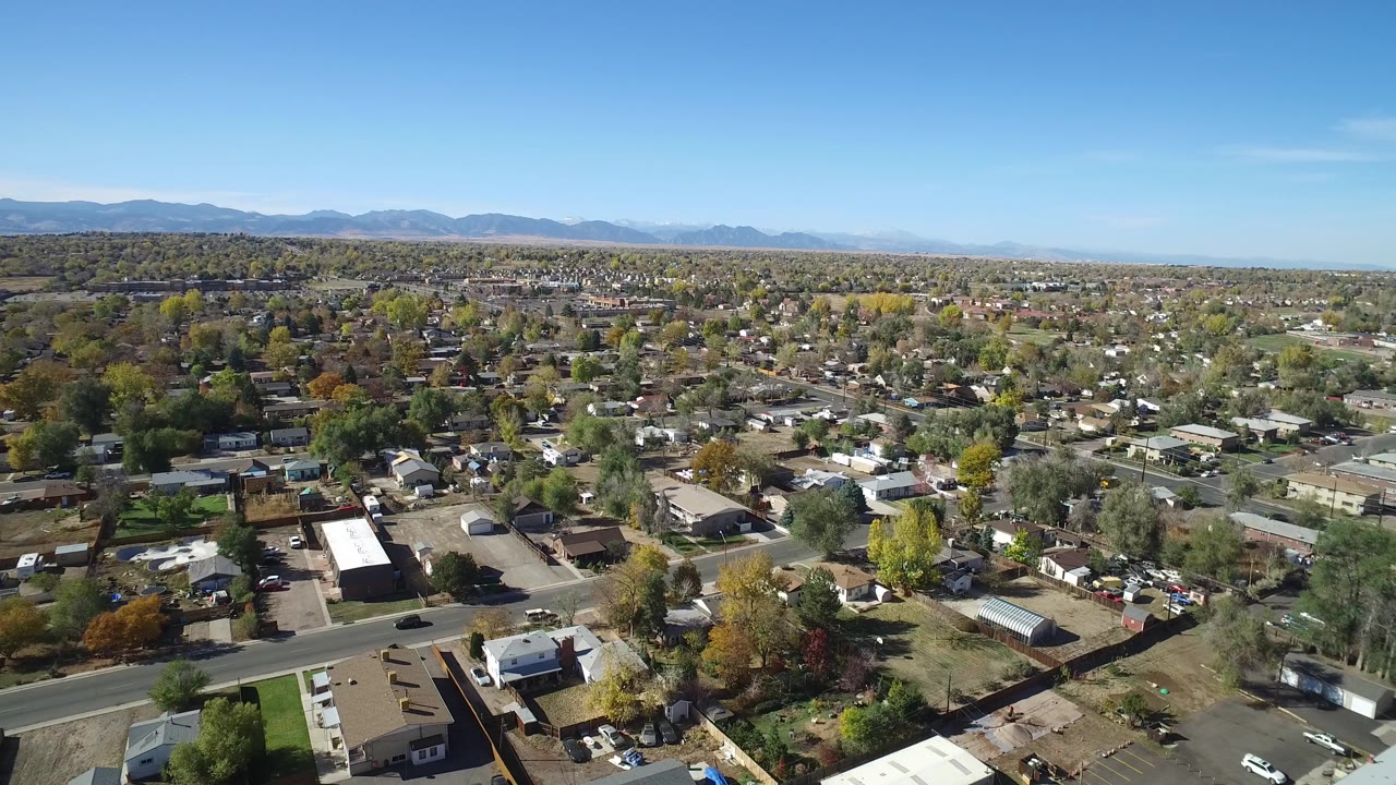 Aerial view over a residential neighborhood with streets, trees, and distant mountains.