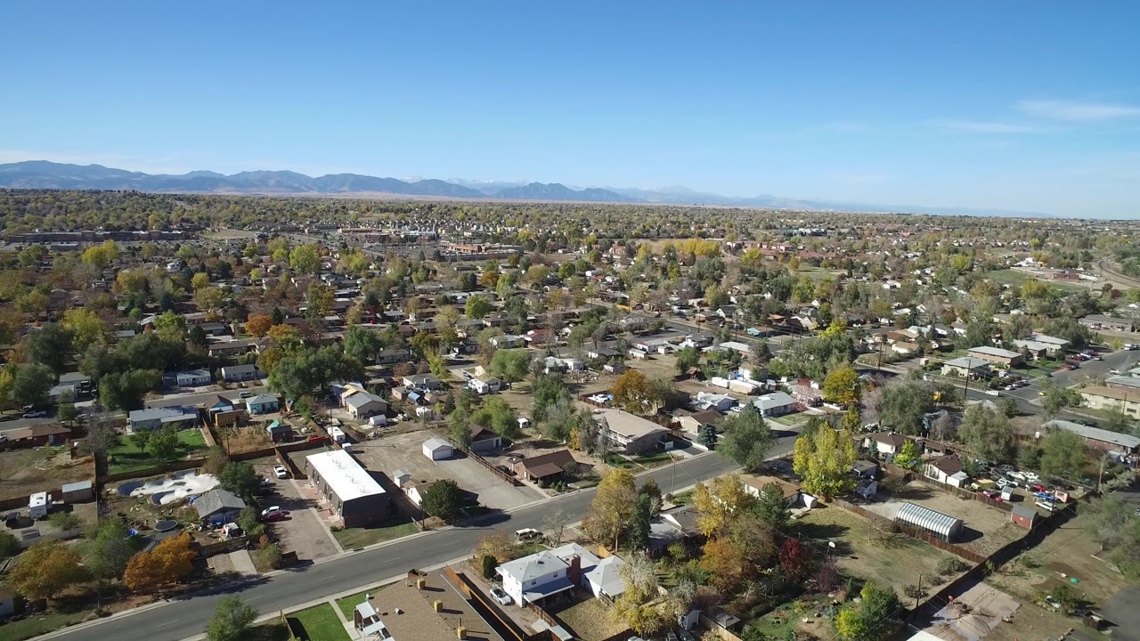 Aerial view over suburban homes, streets, trees, and distant mountains.
