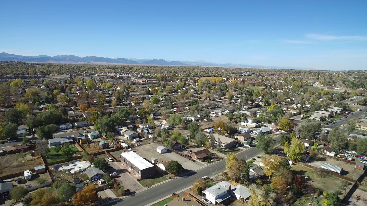 Wide aerial frame over Hidden Lake, Colorado, showing detached homes, intersecting roads, tree cover, distant mountains, blue sky, and no visible people.