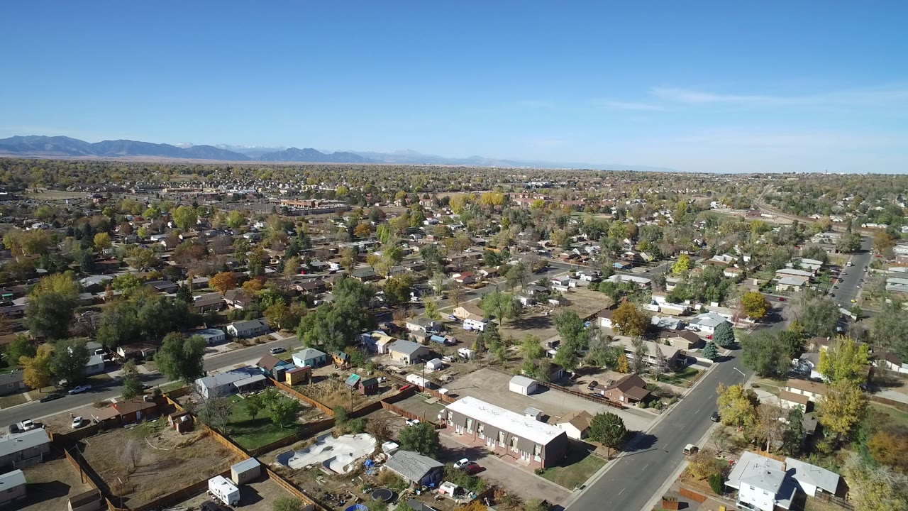 Aerial view over suburban homes, streets, trees, and distant mountains.