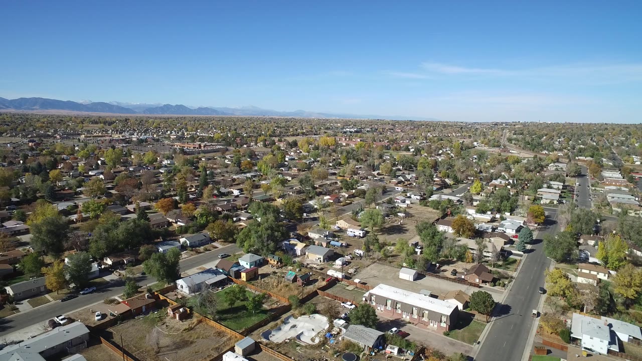 Second aerial frame in Hidden Lake, Colorado showing rooftops and backyards spread below a straight residential road, with a clear sky and no visible people.