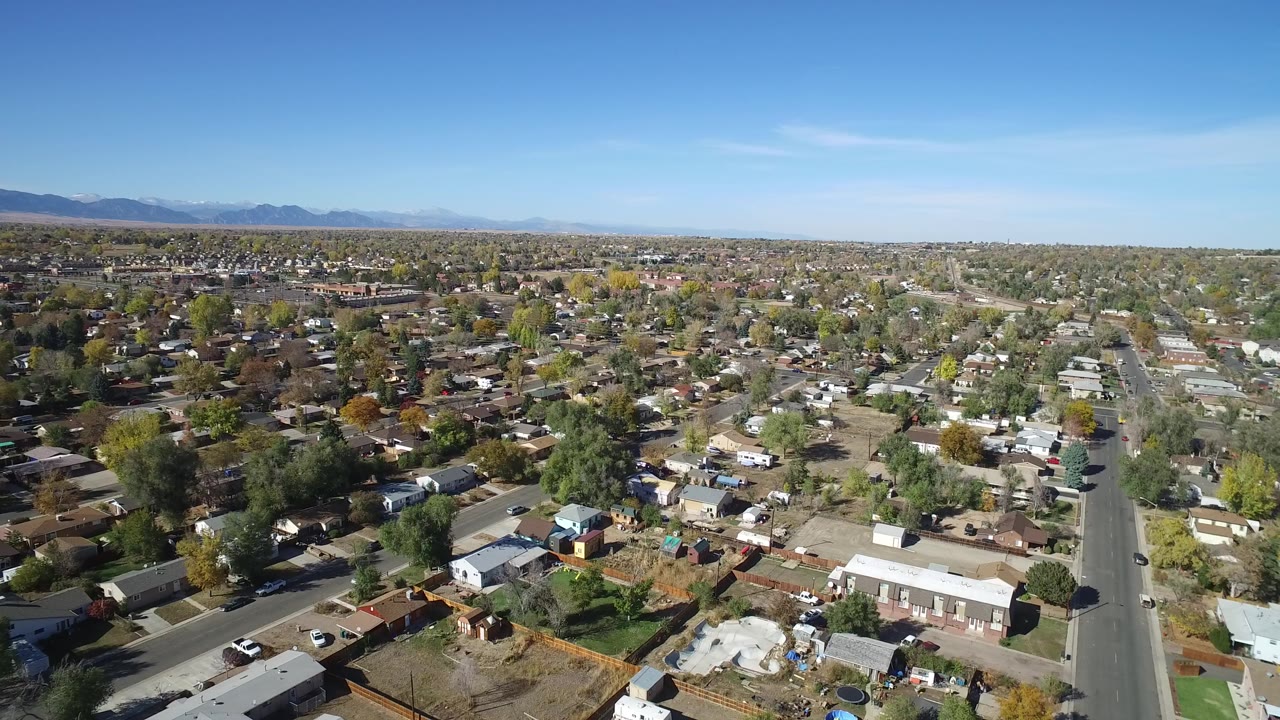 High aerial view over residential streets, rooftops, trees, and distant mountains.
