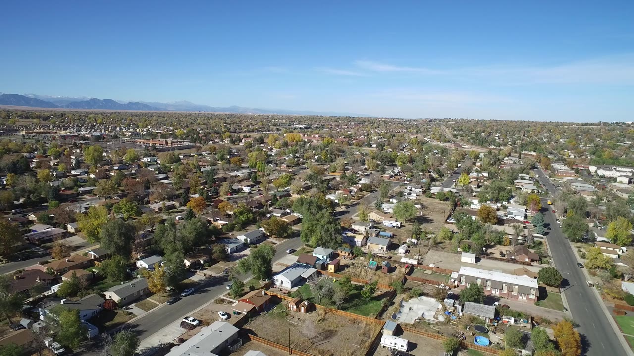Opening aerial frame over Hidden Lake, Colorado with detached homes, tree-lined streets, distant mountains, and no visible people.