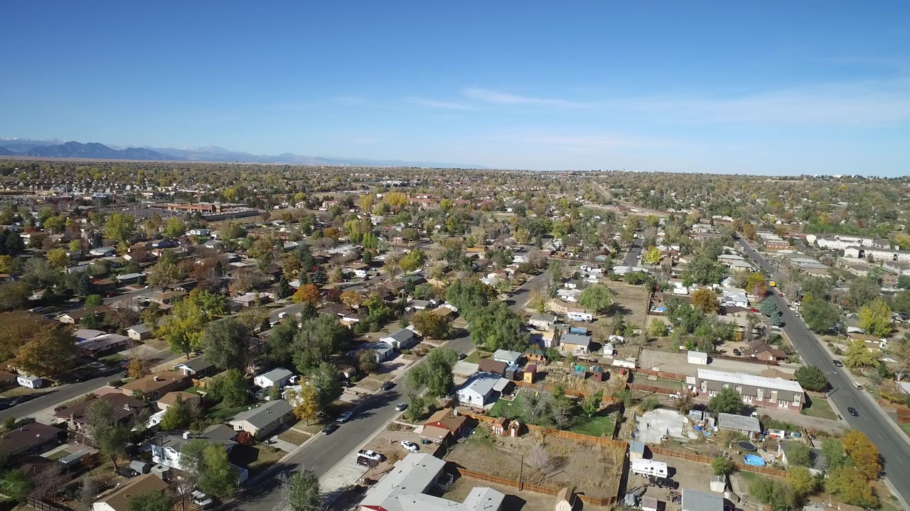 Aerial view over suburban homes, streets, trees, and distant mountains.
