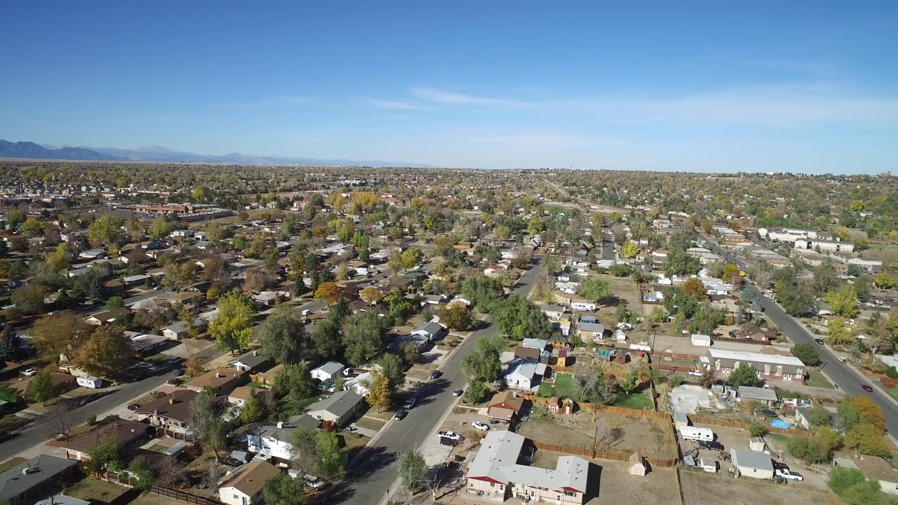 Wide aerial view over residential streets, rooftops, trees, and distant mountains.