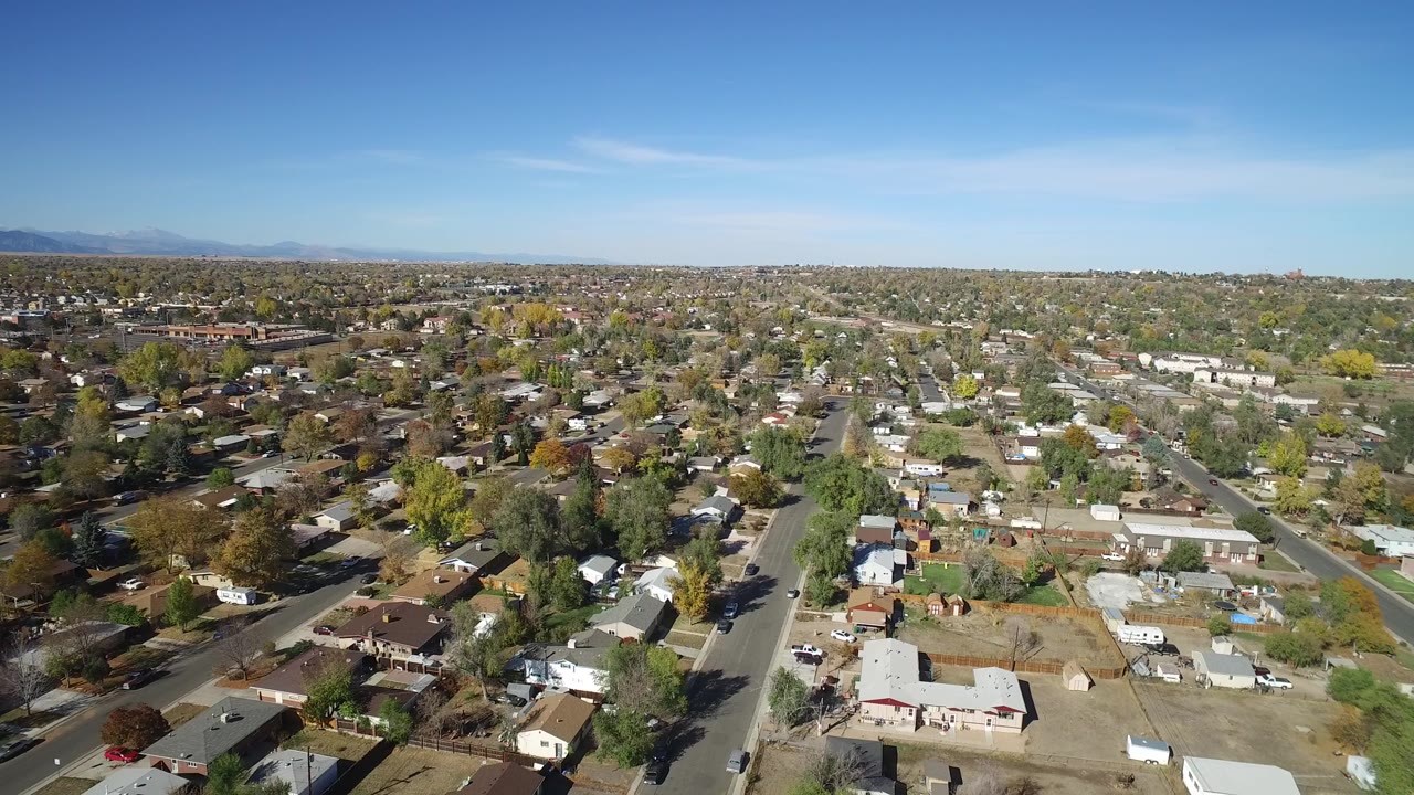 High aerial view of Hidden Lake, Colorado with rooftops, gridded streets, trees, distant mountains, and no visible people at the opening moment.
