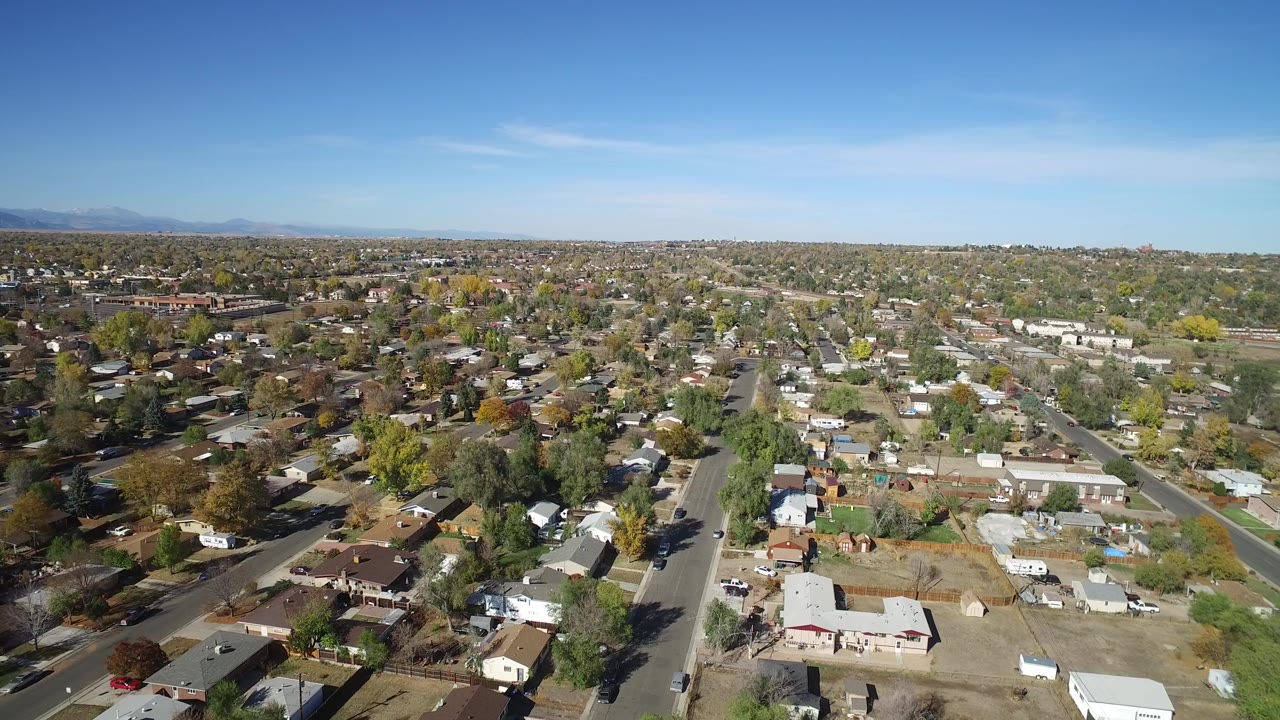 Wide aerial neighborhood view with rooftops, roads, and open sky.