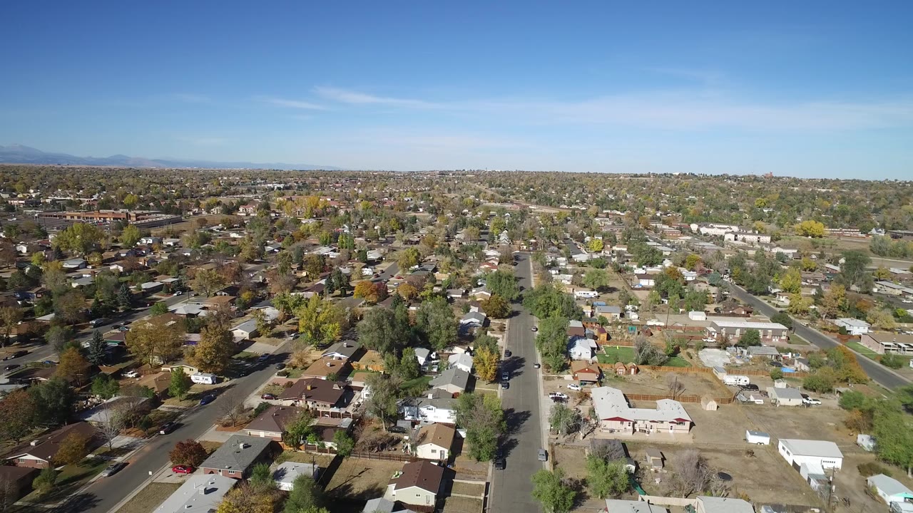 High aerial view over suburban streets and houses beneath a blue sky.