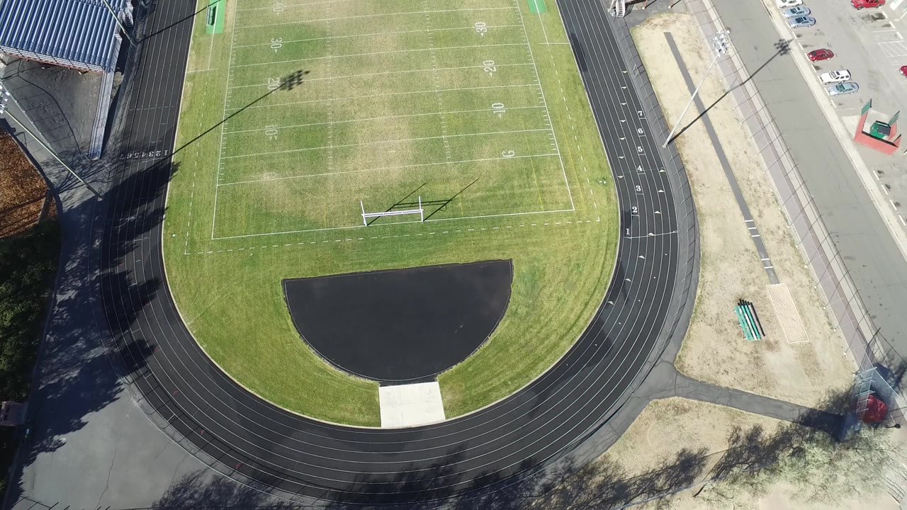 Overhead football field with track, bleachers, parking, and goalposts.