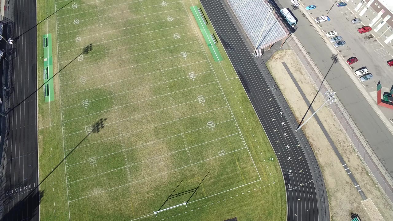 Overhead view of an empty football field beside a track and parking lot.