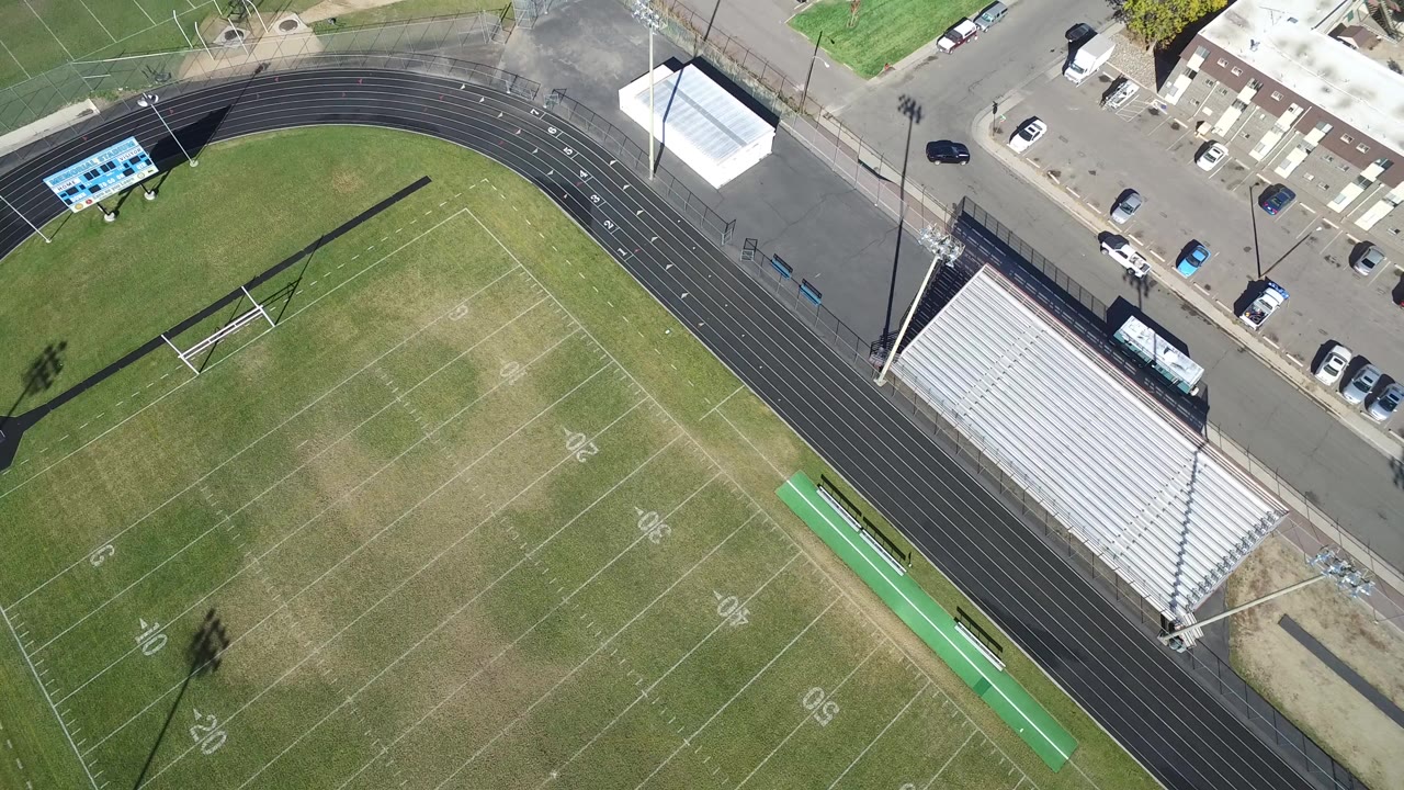 Aerial view of an empty football field, running track, bleachers, and parking lot.