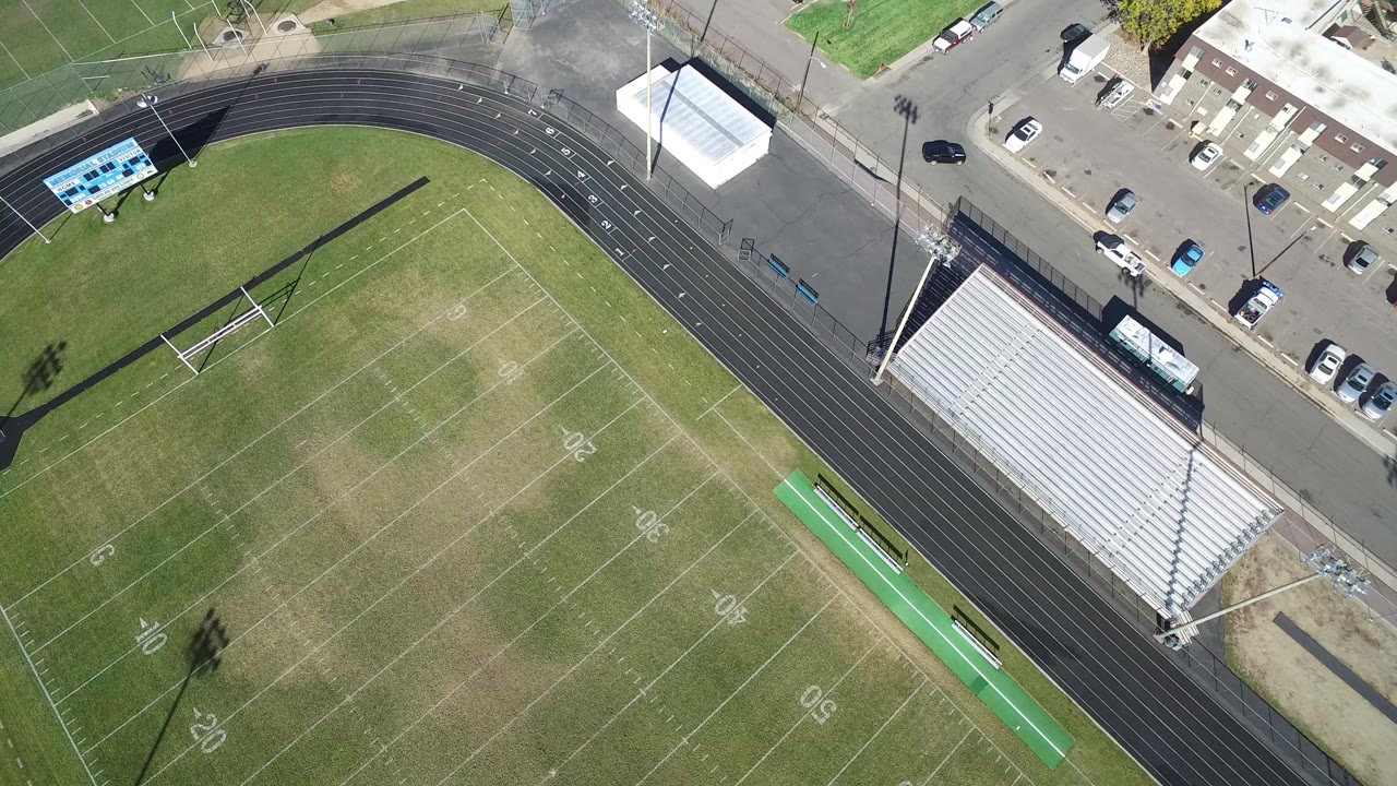 Aerial frame in Hidden Lake, Colorado, showing the field shifted slightly across the view, with the track curve, bleachers, parked cars, and no visible people.