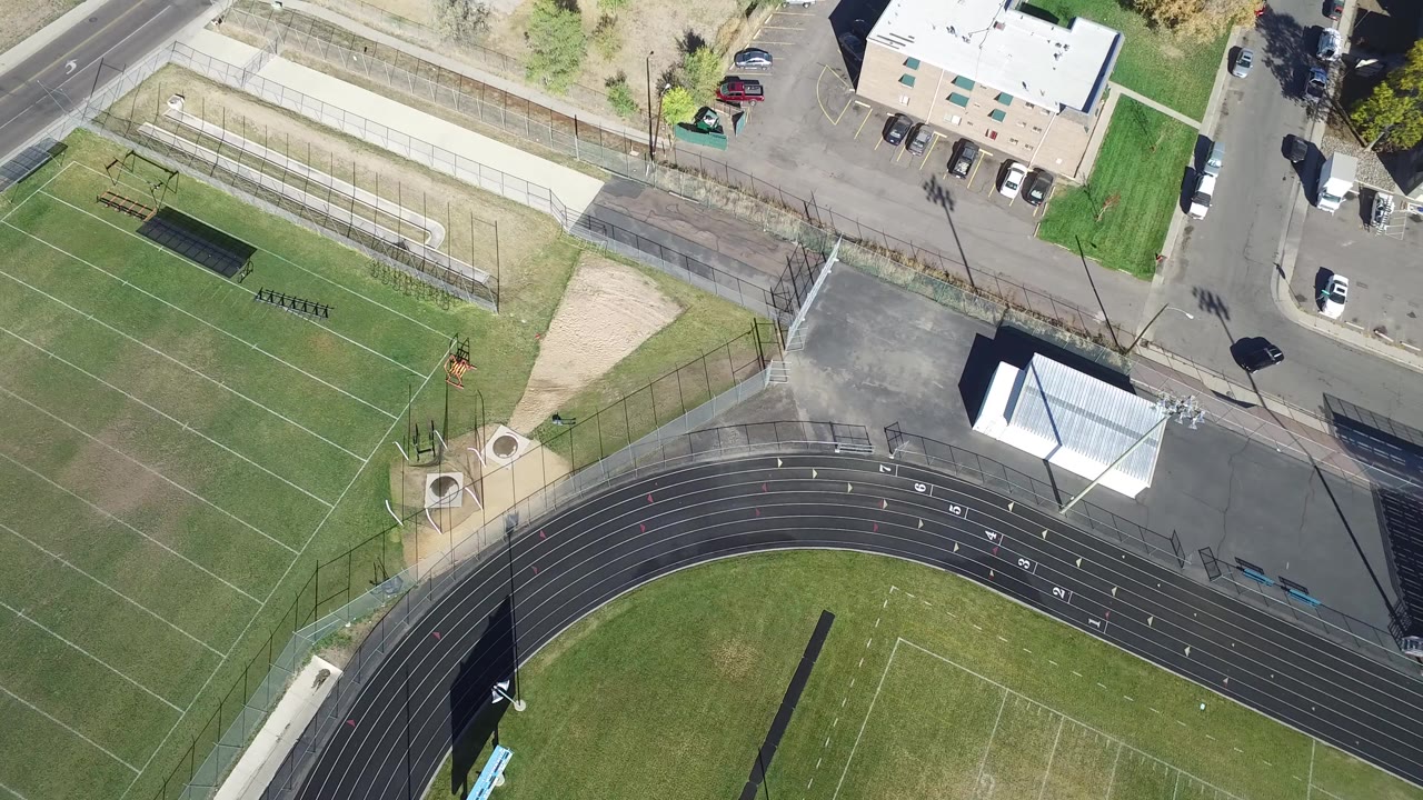 Overhead view of running track, sports fields, roads, buildings, and parked cars.