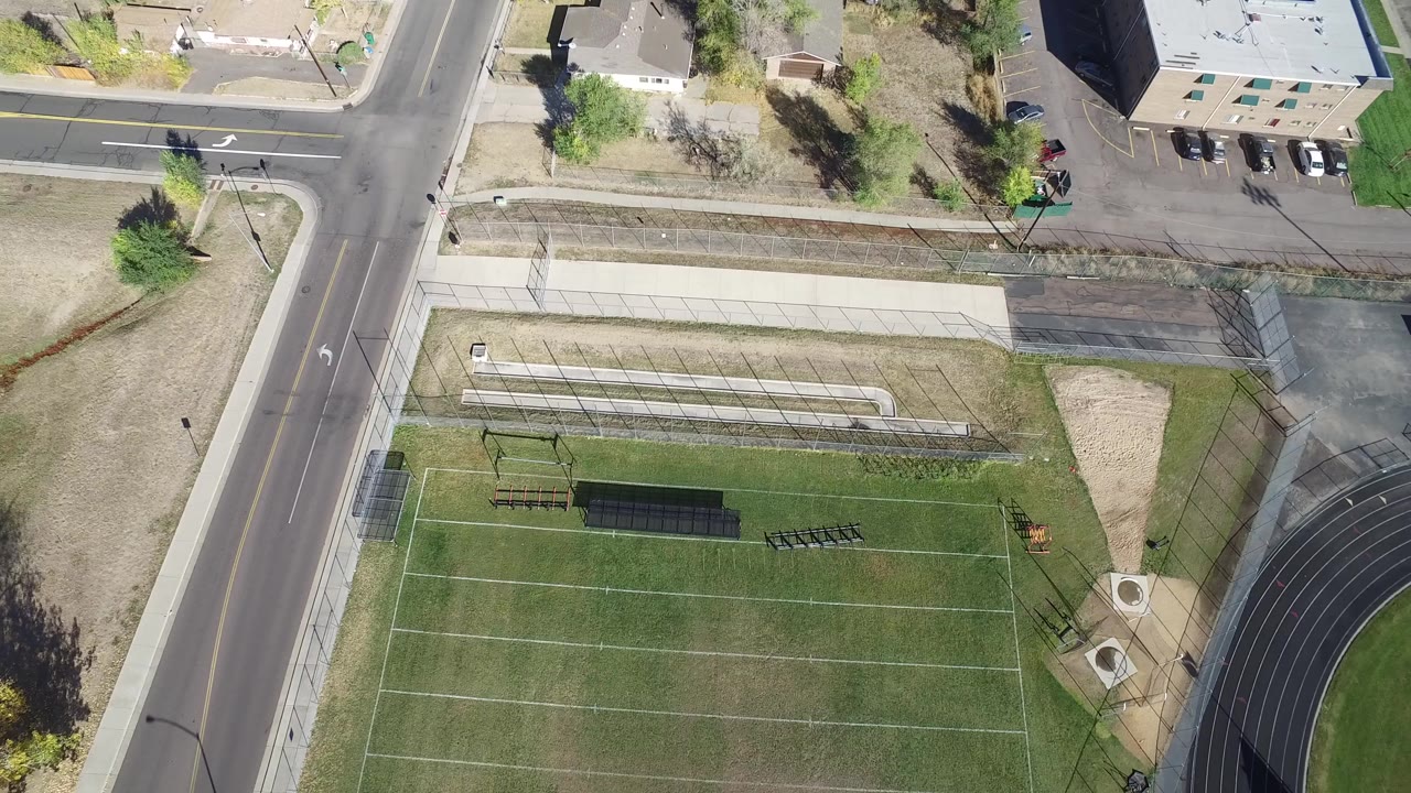 Overhead view of a fenced sports field beside roads and sidewalks.