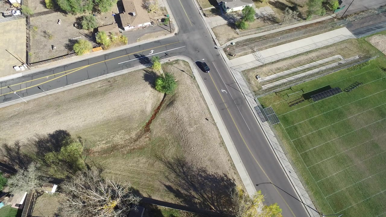 Aerial frame in Hidden Lake, Colorado with the intersection shifted slightly in view, a dark car near the right road, open grass, sidewalks, and no visible people.