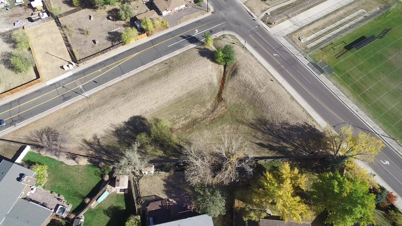 Overhead aerial frame in Hidden Lake, Colorado showing intersecting roads, a dry open lot, residential rooftops, green lawns, trees casting long shadows, and no visible people.