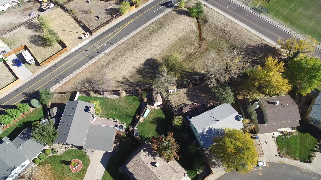 Top-down aerial frame over Hidden Lake, Colorado, showing several private homes, lawns, driveways, trees, a curved street, a two-lane road, and no visible people.