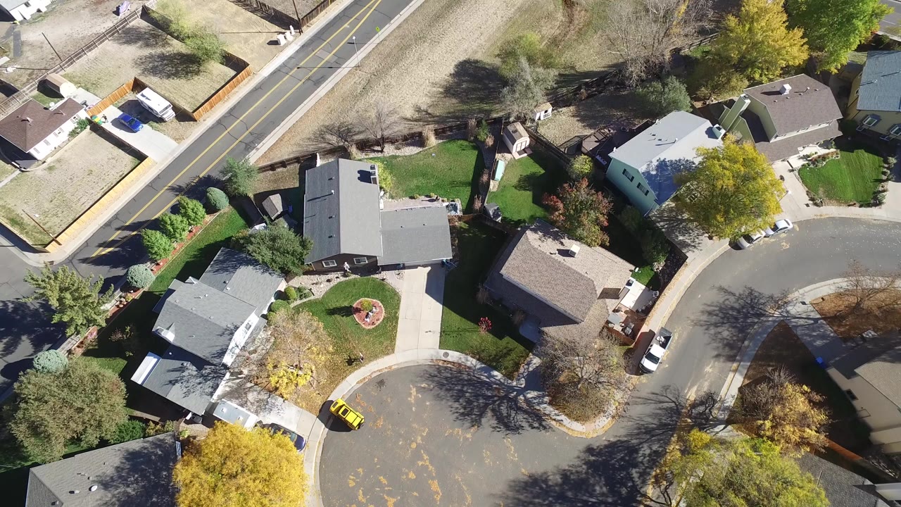 Overhead view of a residential cul-de-sac with houses, trees, lawns, and parked cars.