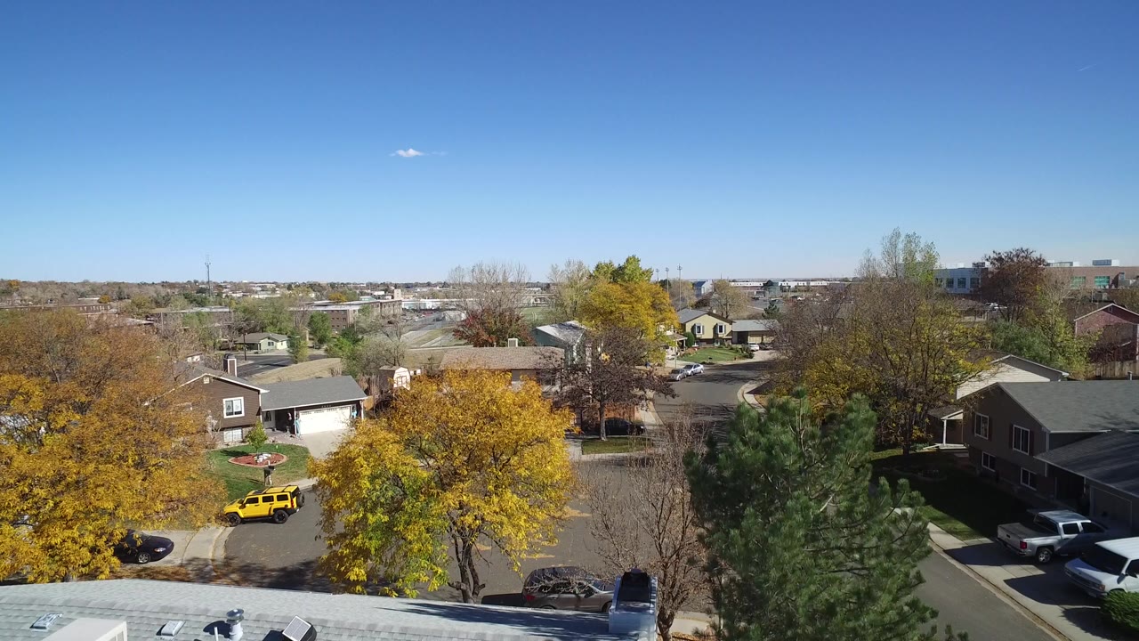 Aerial frame in Hidden Lake, Colorado, looking across houses, a curving residential street, driveways, autumn trees, and no visible people.