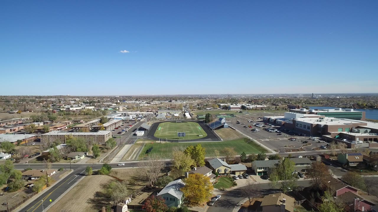Aerial view of a school sports field, roads, houses, and blue sky.