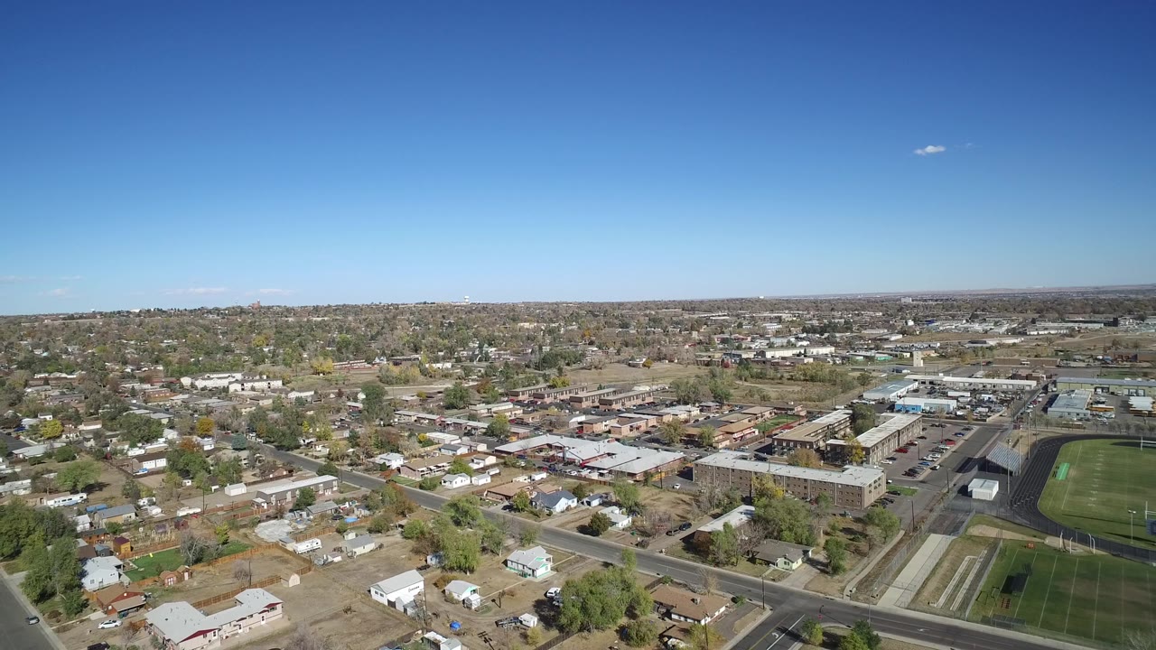 Suburban aerial panorama with houses, commercial-looking buildings, roads, and clear sky.
