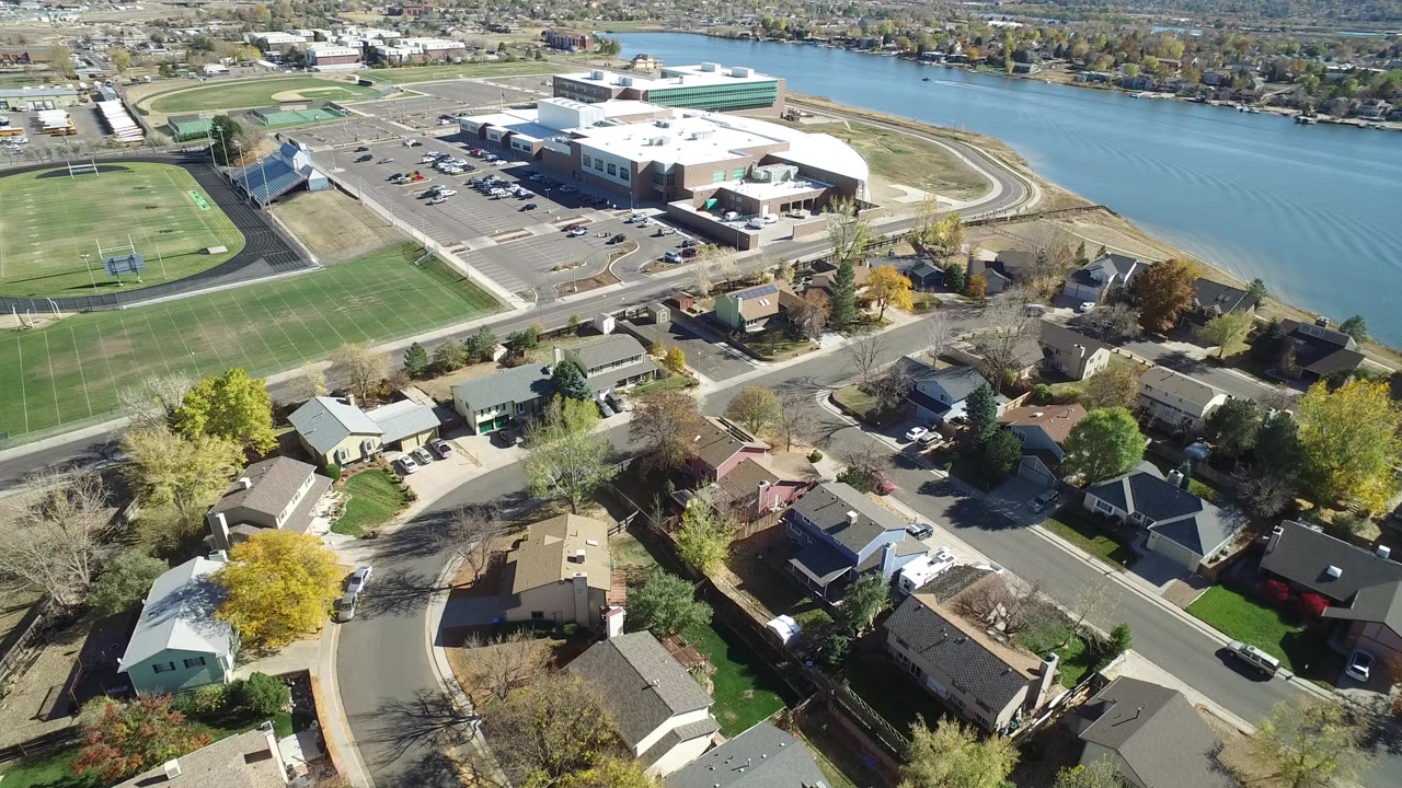 Aerial view of houses, a sports field, a large waterfront building, and lake water.