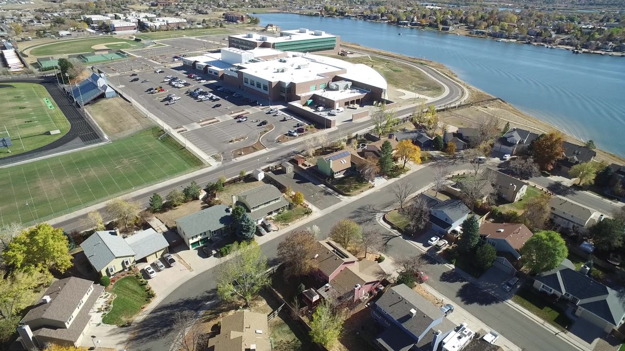 Aerial view of homes, sports fields, a large building, parking lot, and water.