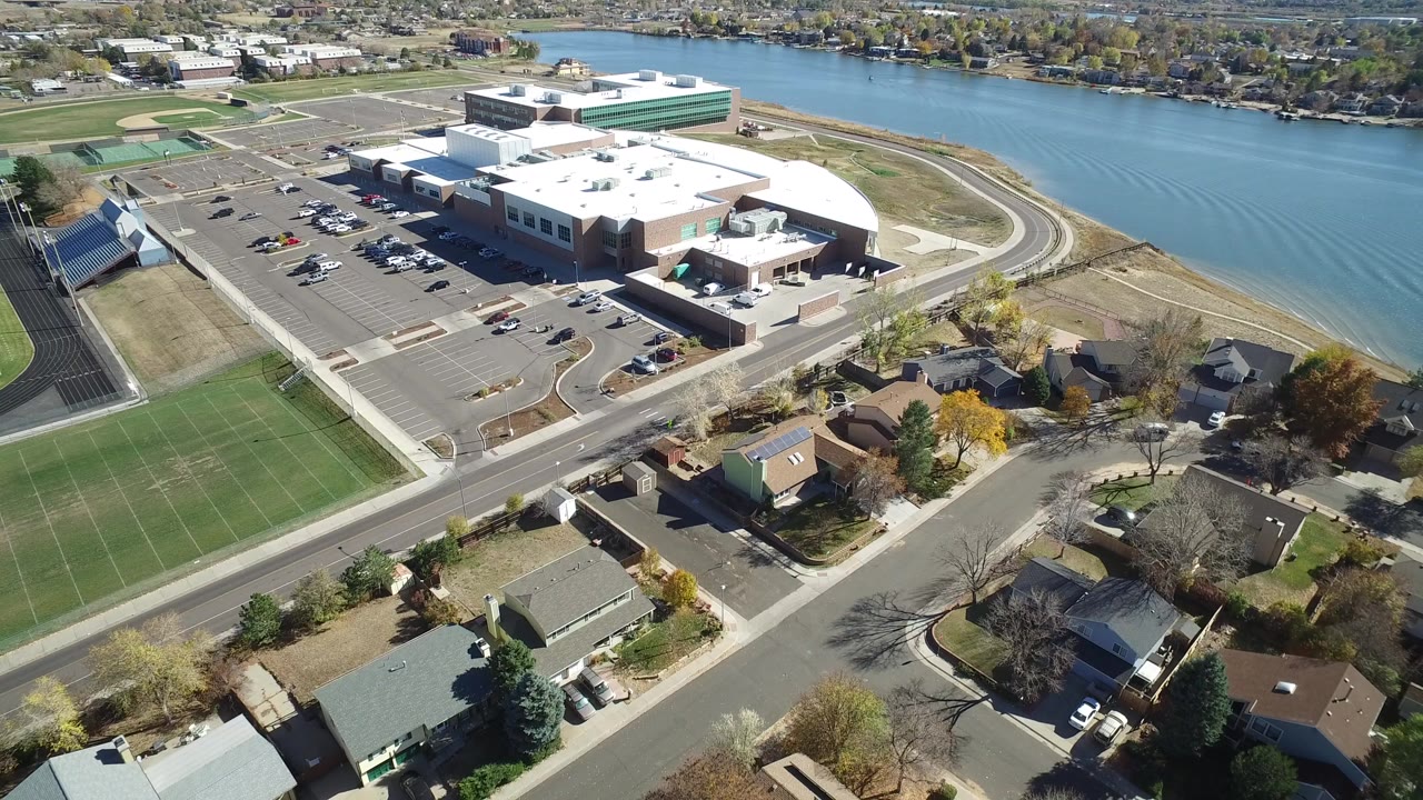 Aerial view of a public complex beside water, sports fields, roads, and homes.