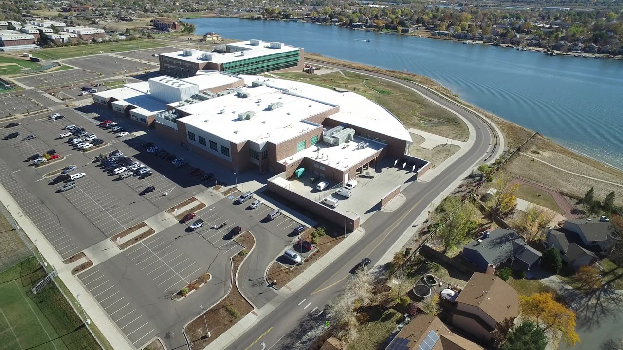 Aerial view in Hidden Lake, Colorado with the commercial building centered, the parking lot to the left, a road wrapping the site, and river water across the top of frame.