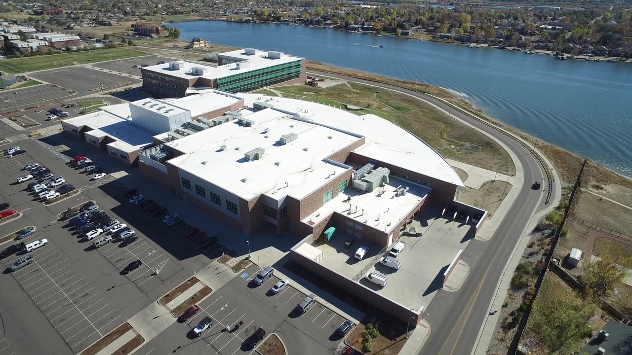 Aerial view of parking lots, a white-roofed complex, and a curved lakeside road.